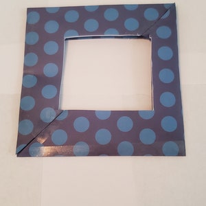 May include: A blue and gray picture frame with a white inner border and a polka dot pattern. The frame is made of cardboard and has a simple design.