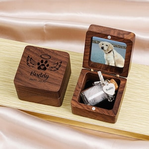 May include: A wooden pet memorial box with a photo frame and a small glass bottle. The box is engraved with a paw print, wings, and the name "Buddy" with the years 2009-2025. The box is open, revealing a photo of a dog.