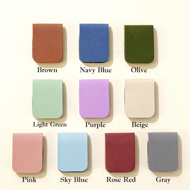 Puede incluir: Una colecci&oacute;n de diez marcadores de p&aacute;gina rectangulares de cuero en varios colores, incluyendo marr&oacute;n, azul marino, oliva, verde claro, morado, beige, rosa, azul cielo, rojo rosa y gris. Cada marcador tiene el nombre del color impreso debajo.