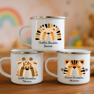 May include: Three white enamel mugs with silver rims, each featuring a colorful animal-themed rainbow graphic. The top mug shows a lion with the text Gro&szlig;er Bruder Daniel, the bottom left a giraffe with Gro&szlig;e Schwester Melanie, and the bottom right a tiger with Kleine Schwester Johanna.