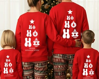 May include: Matching red Christmas pajamas with a white tree design and the text "HO HO HO FROHE WEIHNACHTEN!". The family is wearing patterned pants with red cuffs. A Christmas tree is in the background.