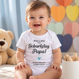 May include: A white short-sleeved baby bodysuit featuring the black printed text Alles Liebe ZUM Geburtstag Papa! with a small light blue heart icon and the additional text MAMA UND ICH LIEBEN DICH printed below the heart.
