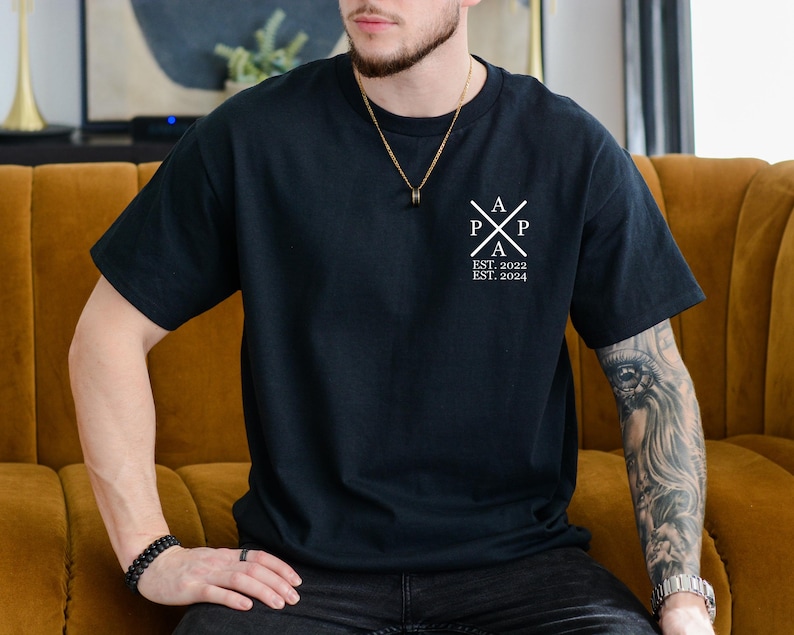 Pu&ograve; includere: Una maglietta nera con un logo bianco che dice "A P P A EST. 2022 EST. 2024". Il logo &egrave; una croce stilizzata con le lettere "A P P A" all'interno.