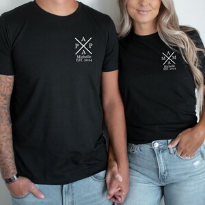 Pu&ograve; includere: Due magliette nere con testo bianco. La maglietta a sinistra dice "Papa" con una croce e il testo "Michelle Est. 2004". La maglietta a destra dice "Mama" con una croce e il testo "Michelle Est. 2004".