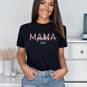 May include: Black t-shirt with the text "MAMA Jacobs 2023" in pink lettering.