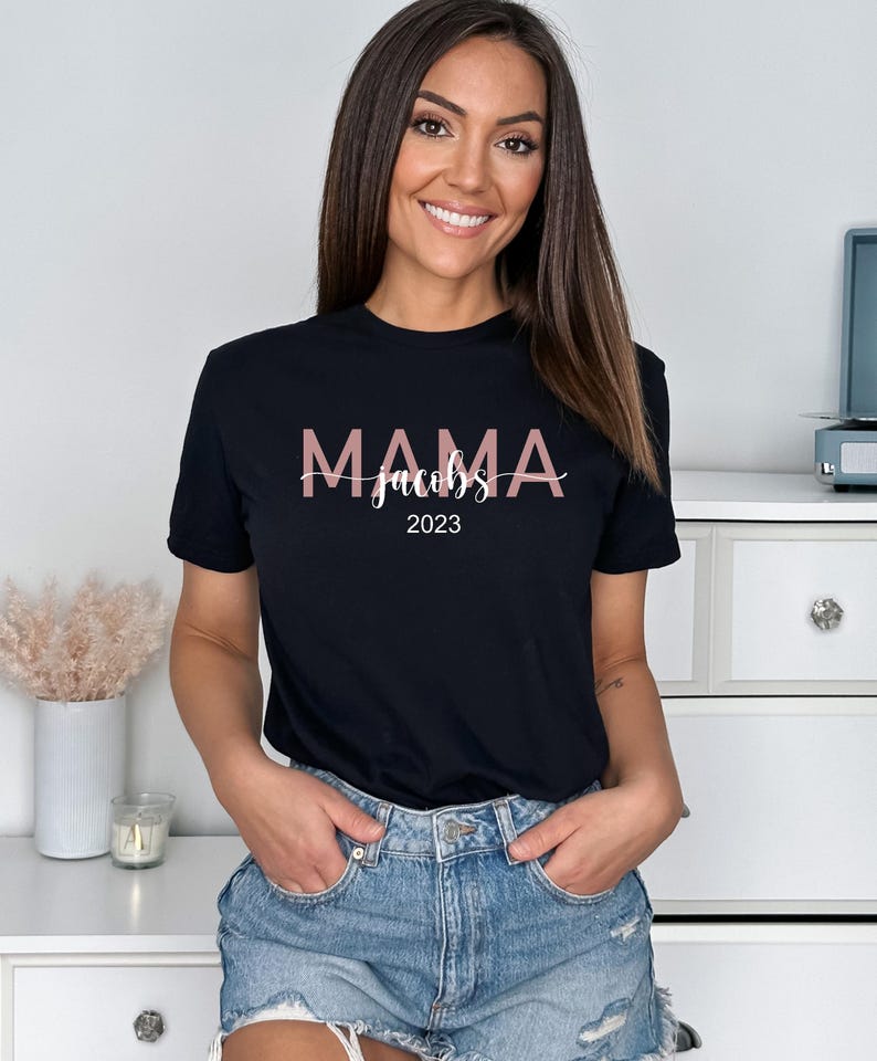 May include: Black t-shirt with the text "MAMA Jacobs 2023" in pink lettering.