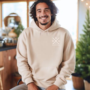 May include: A beige hoodie with a front pocket and a white graphic on the chest. The graphic features the word "DAD" in a crossed design, along with the text "EST. 20/05/24" and "Love & Black Dads".