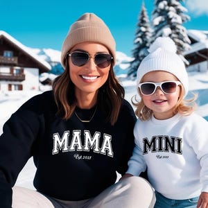 Może przedstawiać: Kobieta i dziecko w pasujących bluzach z napisem "MAMA" i "MINI" w białych literach. Bluzy mają również napis "Est. 2021". Kobieta ma na sobie beżową czapkę i okulary przeciwsłoneczne, a dziecko białą czapkę i okulary przeciwsłoneczne.