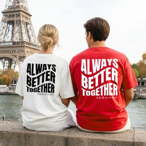 Könnte beinhalten: Ein Paar trägt passende T-Shirts mit dem Text "ALWAYS BETTER TOGETHER" in Weiß. Ein Shirt ist weiß, das andere rot. Das Datum "S&M 31-12-2016" ist darunter aufgedruckt. Im Hintergrund ist der Eiffelturm zu sehen.