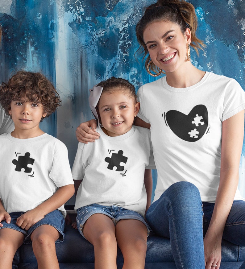 May include: A family wearing white t-shirts with black puzzle piece designs. The adult is wearing a shirt with a heart shape and two puzzle pieces inside. The children are wearing shirts with a single puzzle piece. The family is sitting on a blue couch.