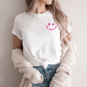 Peut inclure: T-shirt blanc avec un graphique de smiley rose et le texte "Girl Mom Era".