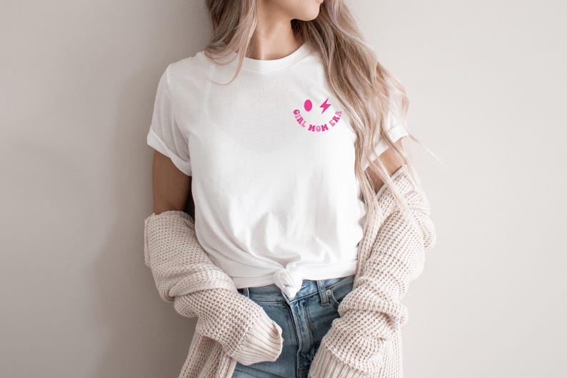 Peut inclure: T-shirt blanc avec un graphique de smiley rose et le texte "Girl Mom Era".