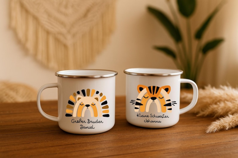 May include: Two white enamel mugs with silver rims. The left mug features a stylized lion graphic with a rainbow mane and the text Gro&szlig;er Bruder Daniel. The right mug features a stylized tiger graphic with a rainbow body and the text Kleine Schwester Johanna.