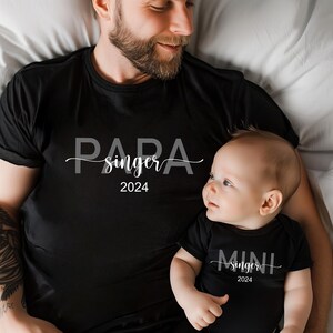 May include: A black t-shirt with the text "Papa singer 2024" and a black bodysuit with the text "Mini singer 2024".