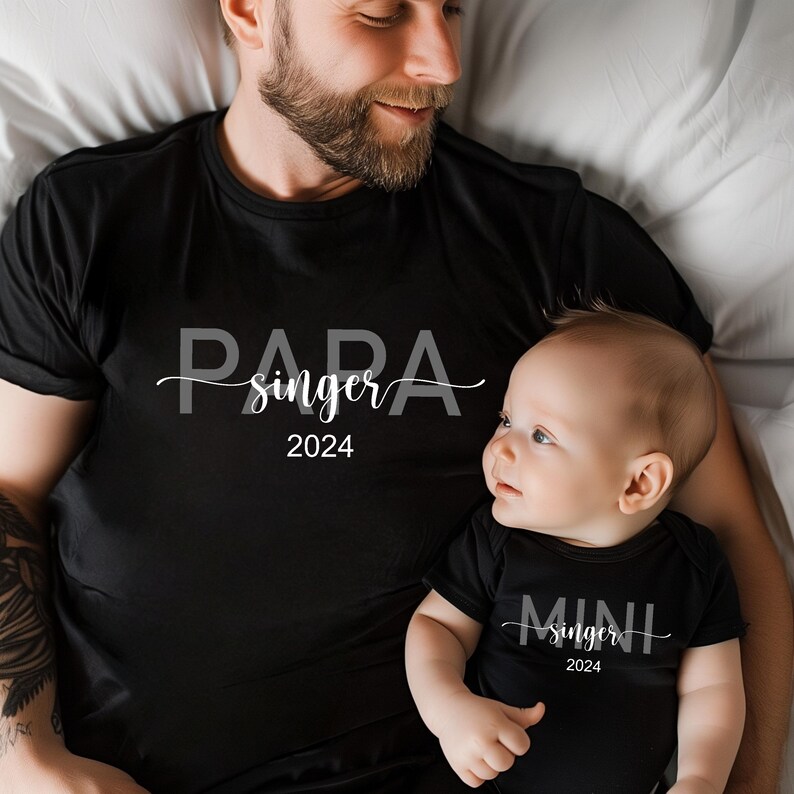 May include: A black t-shirt with the text "Papa singer 2024" and a black bodysuit with the text "Mini singer 2024".