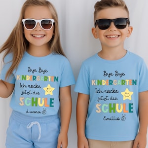 Puede incluir: Dos ni&ntilde;os con camisetas azul claro con el texto "Bye Bye Kindergarten" y "Ich rocke jetzt die SCHULE". Las camisetas tienen un gr&aacute;fico de estrella y los nombres "Luana" y "Emillio". Ambos ni&ntilde;os llevan gafas de sol.