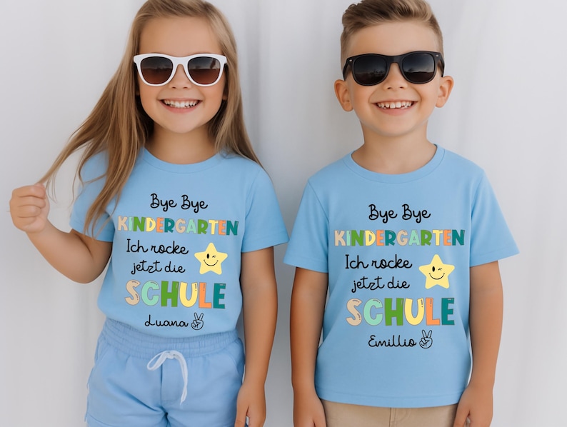 Puede incluir: Dos ni&ntilde;os con camisetas azul claro con el texto "Bye Bye Kindergarten" y "Ich rocke jetzt die SCHULE". Las camisetas tienen un gr&aacute;fico de estrella y los nombres "Luana" y "Emillio". Ambos ni&ntilde;os llevan gafas de sol.