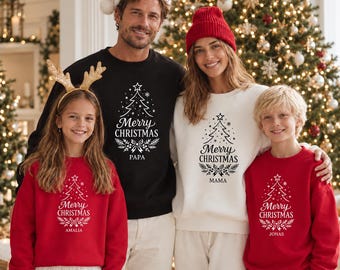 May include: A family wearing matching sweatshirts with a white graphic of a Christmas tree and the text Merry Christmas. The black sweatshirt says Papa, the white one says Mama, and the red ones say Amalia and Jonas respectively.