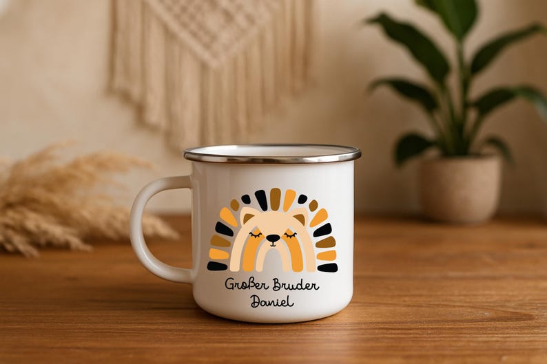 May include: A white enamel mug with a silver rim featuring a graphic of a stylized lion with a rainbow-shaped mane in shades of yellow, brown, and black. Below the lion, the text reads Gro&szlig;er Bruder Daniel in a black, rounded script font.