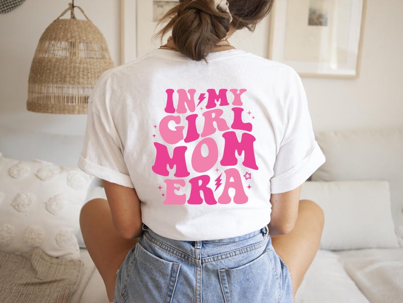 Peut inclure: T-shirt blanc avec un motif rose et blanc qui dit "In My Girl Mom Era" avec un &eacute;clair et des &eacute;toiles.