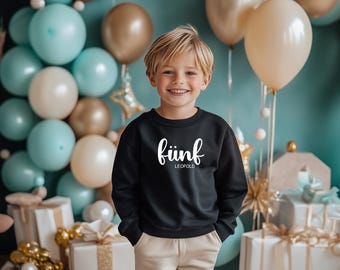 May include: A young boy wearing a black sweatshirt with the text "fünf LEOPOLD" in white. He is standing in front of a blue background with balloons and wrapped gifts.