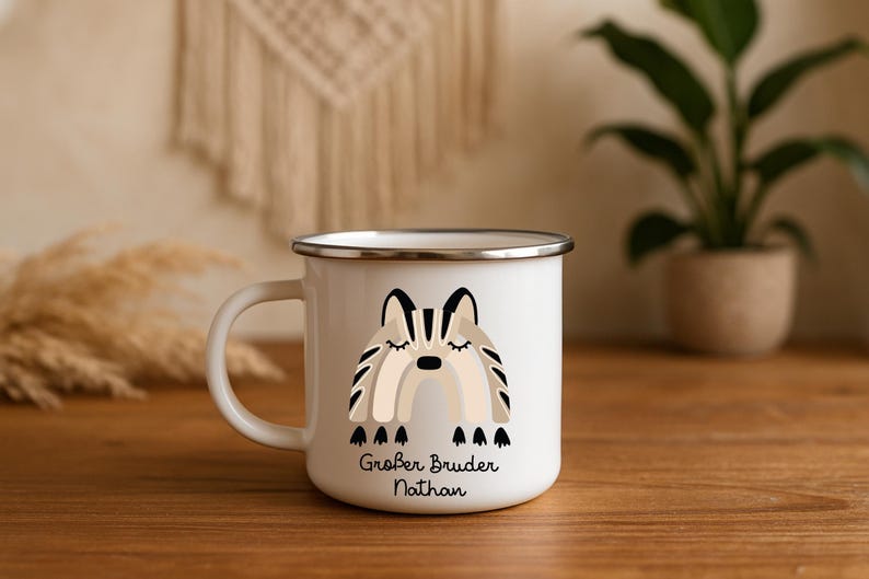 May include: A white enamel mug with a silver rim and a handle on the left side. The front features a graphic of a stylized rainbow in shades of beige, brown, and black, with the German text "Gro&szlig;er Bruder Nathan" printed in black below it.