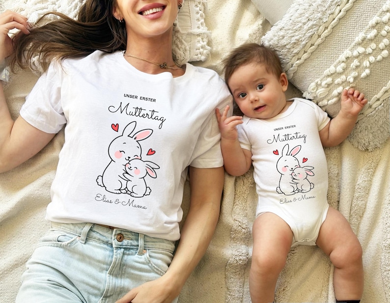 Puede incluir: Conjunto de camiseta blanca y body para beb&eacute;, con un dise&ntilde;o de conejito de dibujos animados y el texto "UNSER ERSTER Muttertag", as&iacute; como los nombres "Elias & Mama". El dise&ntilde;o incluye corazones rojos. El adulto lleva una camiseta, el beb&eacute; un body.