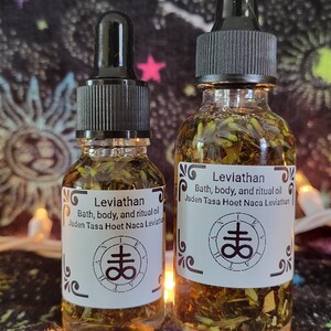 May include: Two glass bottles of Leviathan bath, body, and ritual oil with black droppers. The labels feature the text "Leviathan" and "Jaden Tasa Hoet Naca Leviathan" along with a symbol. The bottles contain a golden liquid with herbs.