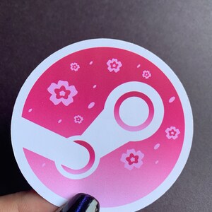 May include: A pink and white round sticker with a stylized white Steam logo and pink flowers. The background is a gradient of pink.