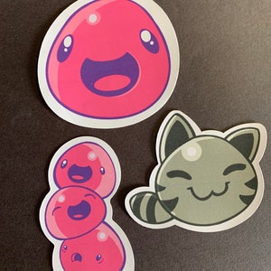 May include: Three stickers featuring cartoon characters. The first sticker is a pink slime with a happy face. The second sticker is a stack of three pink slimes with happy faces. The third sticker is a gray cat slime with a happy face.