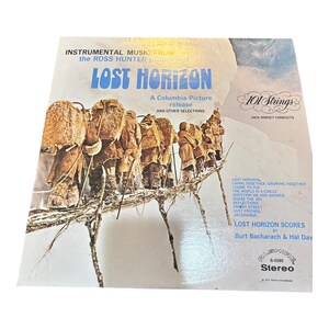 May include: A white ceramic mug with a black handle and the text "But First, Coffee" in a bold, black font. The mug is set against a blurred background, suggesting a cozy setting.