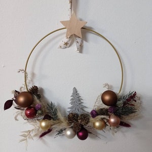 Könnte beinhalten: Ein festlicher Weihnachtskranz mit einem goldenen Metallring als Basis. Der Kranz ist mit braunen, goldenen und roten Kugeln, Tannenzapfen und einem silbernen Glitzertannenbaum geschmückt. Ein Holzstern hängt an einem Band mit goldenen Sternen.