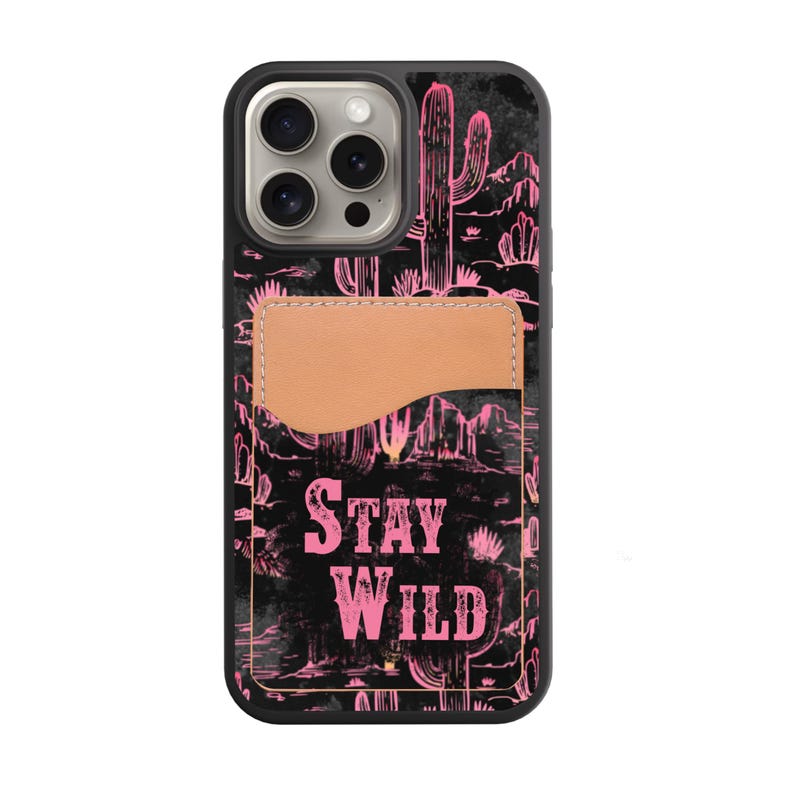 May include: Black phone case with a pink desert landscape design, including cacti and mountains. The case features a tan cardholder and the words "STAY WILD" in pink. The case is designed for a smartphone.