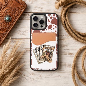 May include: A phone case with a brown and white cowhide pattern and a brown leather cardholder. The case features a playing card design with a cowboy and the words "Long Live Cowgirls."