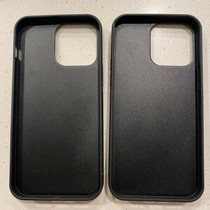 May include: Two black phone cases are displayed side-by-side. The cases have a matte finish and are designed to fit a smartphone. The cases have openings for the camera and other phone features.