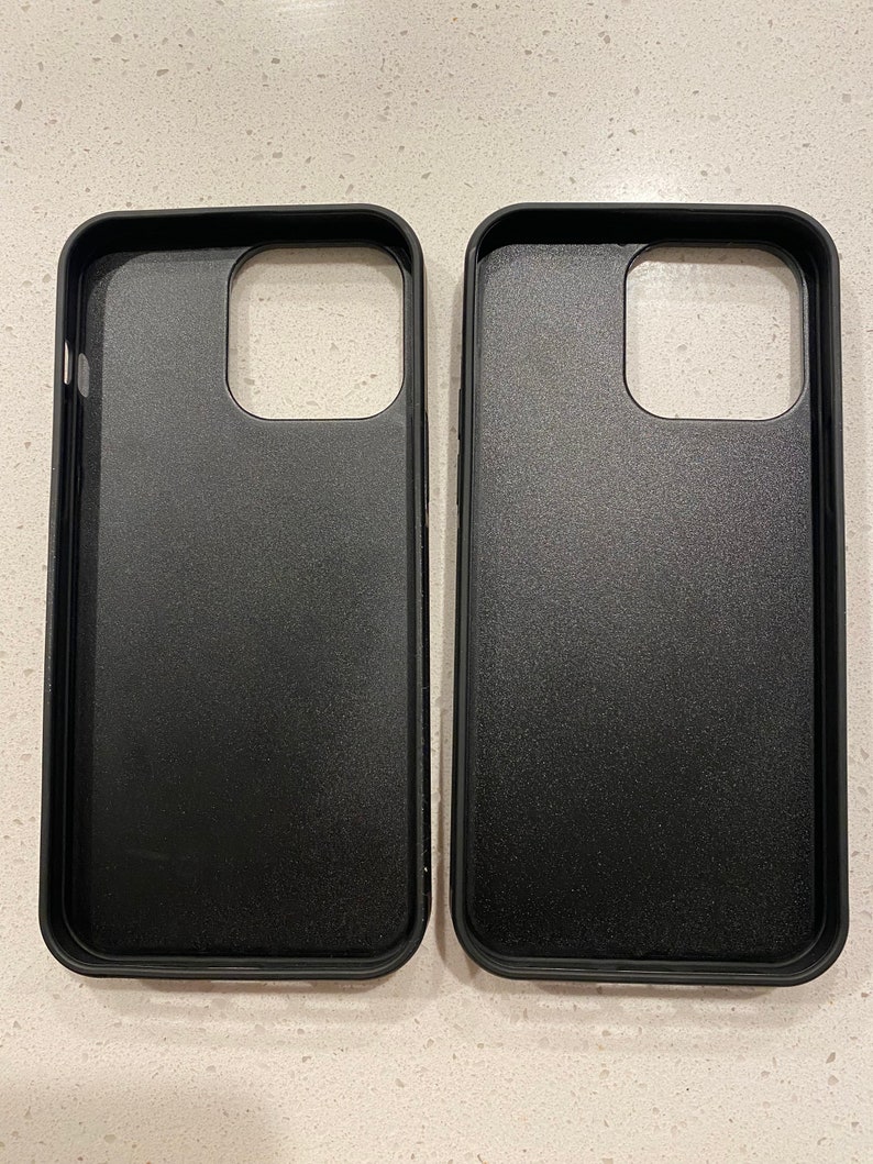May include: Two black phone cases are displayed side-by-side. The cases have a matte finish and are designed to fit a smartphone. The cases have openings for the camera and other phone features.