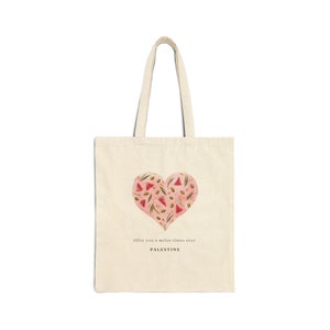 May include: A beige tote bag with a pink heart design featuring watermelon slices and green leaves. The text "Olive you a melon times over PALESTINE" is printed below the heart.