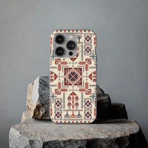 May include: A phone case with a beige background and a red, blue and black geometric pattern. The case has a triple lens camera cutout.