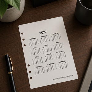 May include: A white paper planner insert featuring a 2027 yearly calendar with twelve months arranged in a grid. The page has five circular binder holes along the left edge and the text WWW.SPARROWHILLFARMS.COM printed at the bottom right corner.