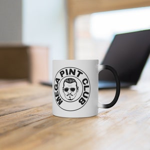 Può includere: Tazza in ceramica bianca con un design circolare nero che presenta il testo "MEGA PINT CLUB" e un'immagine di un uomo dei cartoni animati con occhiali da sole.