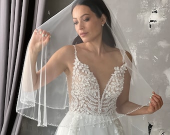 May include: A white bridal veil with a beaded edge, worn by a woman in a white wedding dress with lace detailing.