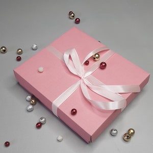 Puede incluir: Una caja de regalo rosa con una cinta de sat&eacute;n blanca atada en un lazo. La caja est&aacute; rodeada de peque&ntilde;as cuentas de colores.