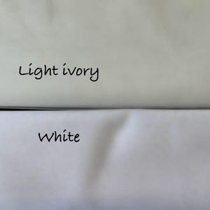 May include: A close-up of two fabric swatches, one light ivory and one white. The words "Light ivory" and "White" are handwritten in black ink above each respective fabric sample. The fabrics are slightly wrinkled.