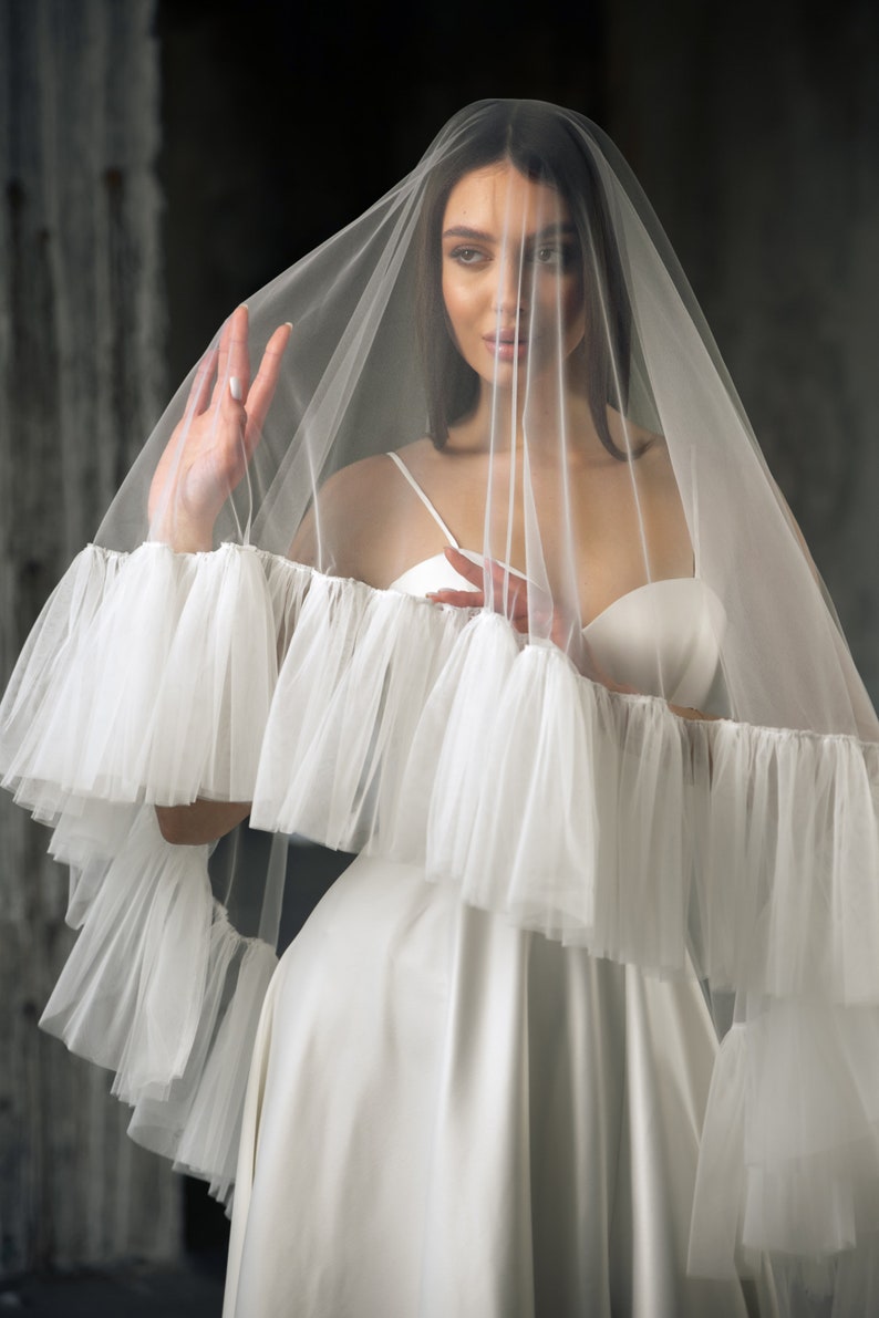Puede incluir: Un velo de novia blanco con un borde con volantes. El velo est&aacute; hecho de tul suave y est&aacute; dise&ntilde;ado para usarse sobre la cabeza y los hombros.