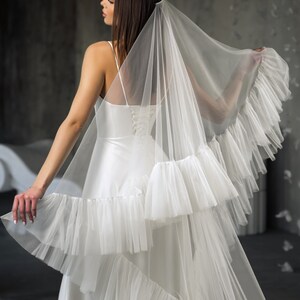 Puede incluir: Un velo de novia blanco con m&uacute;ltiples capas de volantes. El velo est&aacute; hecho de tul suave y tiene un aspecto delicado y rom&aacute;ntico.