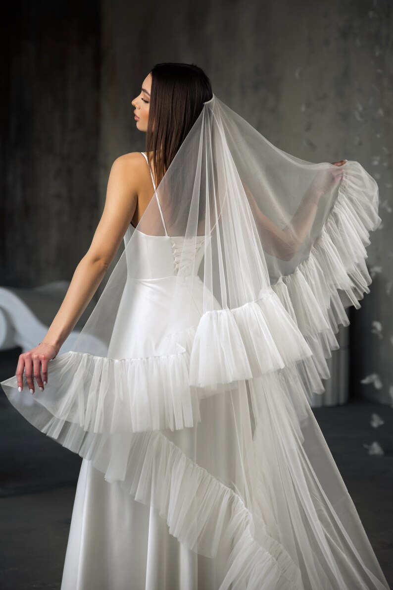 Puede incluir: Un velo de novia blanco con m&uacute;ltiples capas de volantes. El velo est&aacute; hecho de tul suave y tiene un aspecto delicado y rom&aacute;ntico.