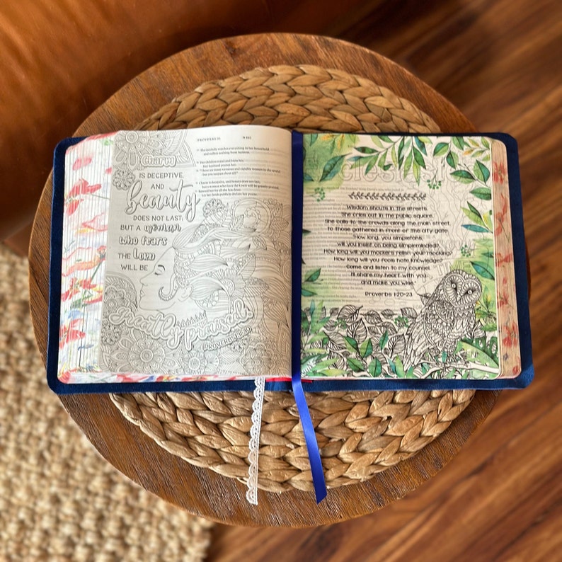 May include: An open book with illustrated pages featuring intricate floral patterns, a profile of a person, and an owl. The left page displays the text Charm is deceptive and beauty does not last, but a woman who fears the Lord will be greatly praised.