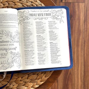 May include: An open book with a blue cover featuring a Tyndale Verse Finder page. The left page displays decorative text including Revelation 22:20, while the right page lists biblical topics like accountability, adultery, and anger with references.
