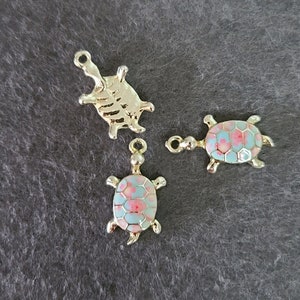Pode incluir: Três pingentes de tartaruga de ouro. Duas das tartarugas têm um design de esmalte azul e rosa. A terceira tartaruga é de ouro liso.