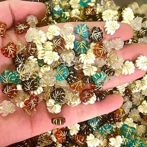 May include: A collection of glass leaf-shaped beads in various colours, including clear, white, teal, brown, and gold. The beads have a gold leaf design and are perfect for jewellery making or crafting.